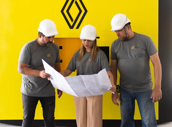 Reunião de obra em equipe Equipe de engenheiros analisando planta em frente a painel amarelo com logotipo