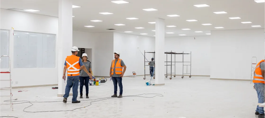 Profissionais com coletes de segurança e capacetes em obra de grande espaço interno