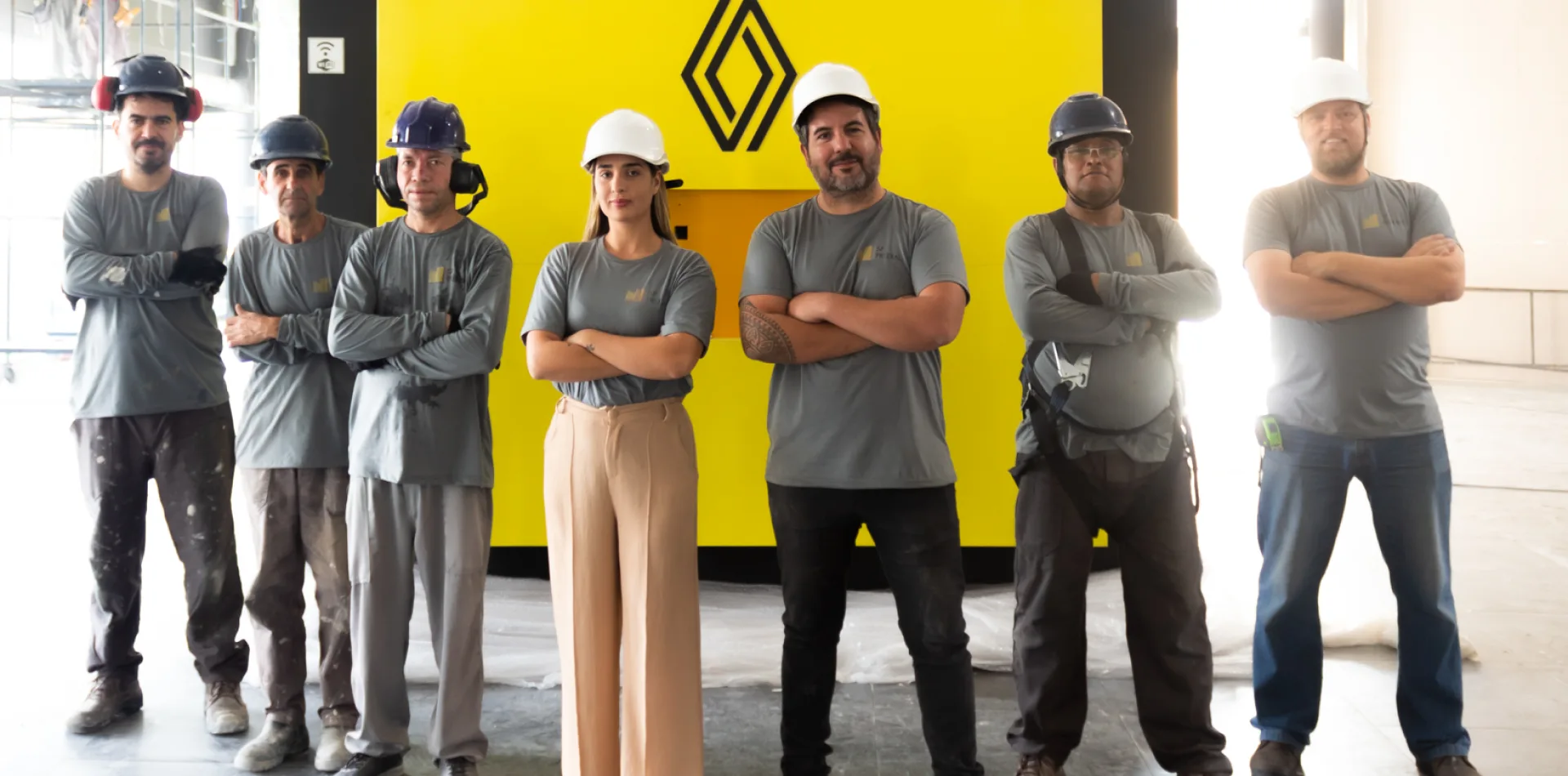 Equipe de profissionais da construção em frente a painel amarelo com logotipo